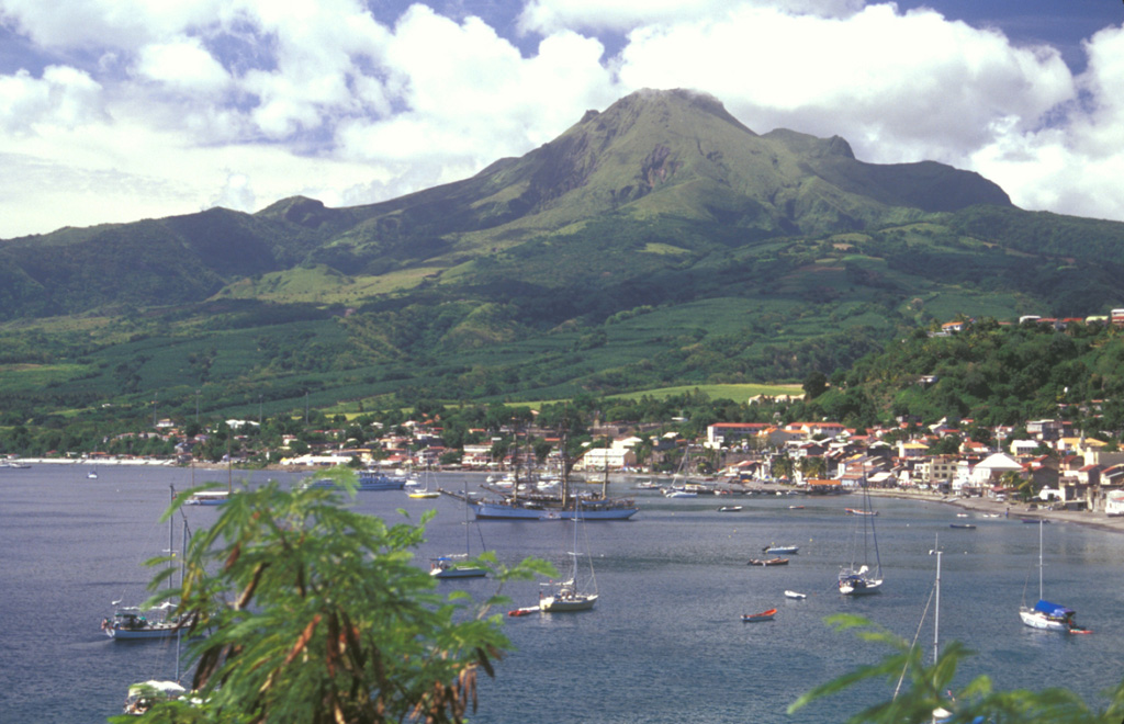 Mount Pelée towers above the city of St. Pierre in northern Martinique a century after the catastrophic eruption that destroyed the city in 1902.  Pelée is the most active volcano of the Lesser Antilles arc, with more than 20 major eruptions during the past 5000 years.  Lava domes formed during the 1902 eruption and one in 1929 form the present summit, which was constructed within a large scarp visible on the lower left horizon that formed when the volcano collapsed about 9000 years ago.   Photo by Lee Siebert, 2002 (Smithsonian Institution).