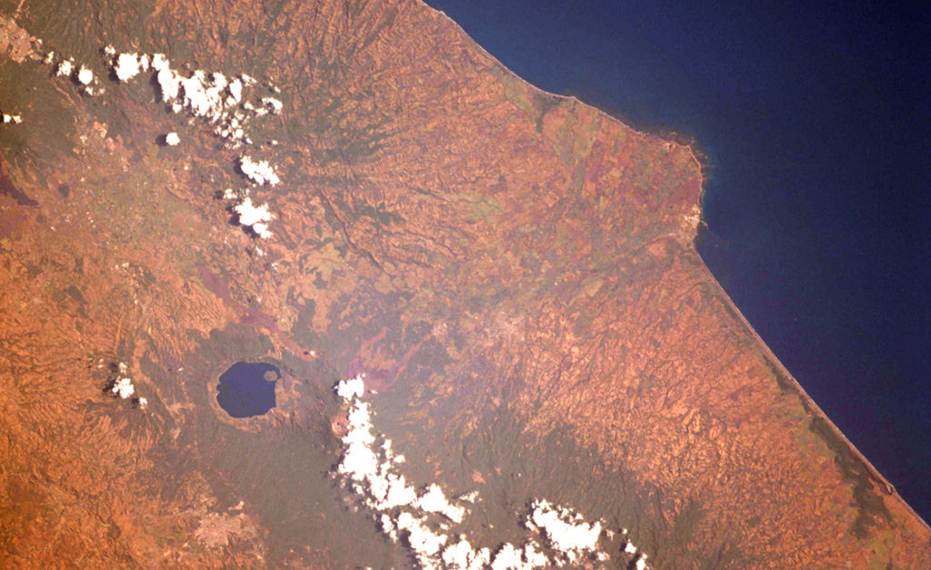 The Acajutla Peninsula is the largest topographic irregularity along a 900-km-long stretch of the Pacific coast between the Gulf of Tehuantepec off Oaxaca, México and the Gulf of Fonseca at the SE tip of El Salvador.  The 20-km-wide peninsula was created by a debris avalanche that traveled nearly 50 km following the late-Pleistocene collapse of Santa Ana volcano, located beneath the cloud bank to the right of Coatepeque lake.  Part of the shallow submarine component of the deposit is visible in this International Space Station image with north to the lower left. NASA International Space Station image ISS004-701-34, 2002 (http://eol.jsc.nasa.gov/).