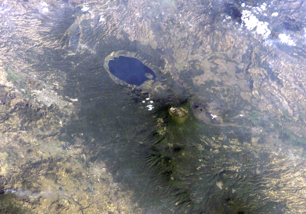 Lake-filled Coatepeque caldera is prominent in this International Space Station image with north to the lower left.  A post-caldera lava dome forms an island at the SW side of the lake.  The nested summit craters of Santa Ana volcano are visible below and to the right of Coatepeque, and the unvegetated cone of Izalco volcano is to the right of Santa Ana.  Small stratovolcanoes of the Sierra de Apaneca form the forested ridge at the bottom right.  The light-colored area at the left-center is the city of Santa Ana, the second largest in El Salvador. NASA International Space Station image ISS004-E-9398, 2002 (http://eol.jsc.nasa.gov/).