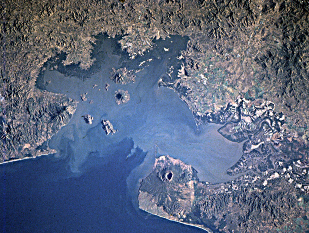 Young volcanoes dot the surface and anchor the shores of the Gulf of Fonseca, which forms the coastline of three countries.  Conchagua volcano occupies the wedge-shaped peninsula (left-center) in eastern El Salvador, while Cosigüina volcano forms the prominent peninsula across the bay in Nicaragua.  Clockwise from the top are the islands of Zacate Grande and El Tigre in Honduras and Meanguera and Conchaguita in El Salvador.  The mouth of the Gulf of Fonseca is about 30 km wide. NASA Space Shuttle image STS82-731-83, 1997 (http://eol.jsc.nasa.gov/).