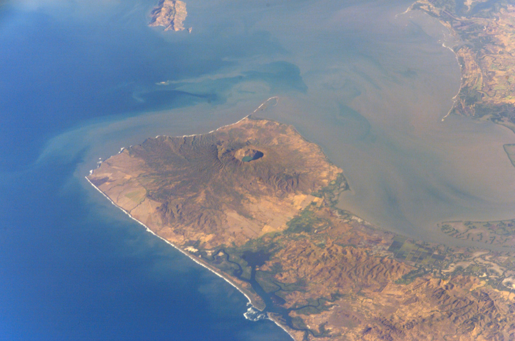 Cosigüina volcano forms the northern half of a 25-km-wide peninsula extending NW-ward into the Gulf of Fonseca.  A 2-km-wide caldera, partially filled by a lake, truncates the summit of the volcano, and the scarp of a larger older caldera is visible to the NW.  Pyroclastic flows from the catastrophic 1835 eruption, the largest in Nicaragua during historical time, reached the Gulf of Fonseca.  The volcanic island of Meanguera in the El Salvador side of the Gulf of Fonseca is visible at the top left. NASA International Space Station image ISS004-E-9143, 2002 (http://eol.jsc.nasa.gov/).