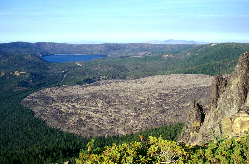 The Big Obsidian Flow covers 2.6 km2 of the floor of Newberry caldera and was emplaced about 1,300 years ago. The eruption began from a vent at the base of the southern caldera wall with a large pumice fall deposit followed by a pyroclastic flow that entered Paulina Lake, and finally with emplacement of the obsidian flow. East Lake lies in the background in this view from the southern caldera rim. Photo by Lee Siebert, 2002 (Smithsonian Institution).