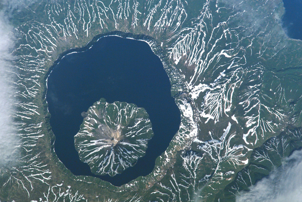 Snow remnants highlight dendritic drainages eroded into pyroclastic flow deposits on the flanks of Tao-Rusyr caldera on Onekotan Island in this NASA Space Shuttle image (with N to the left). The 7.5-km-wide caldera formed about 7,500 years ago during the eruption of 30-35 km3 of tephra, producing one of the largest Holocene eruptions of the Kuril Islands. Subsequently, Krenitzyn Peak was constructed in the NW part of the caldera, reaching a height well above the caldera rim. NASA International Space Station image ISS005-E-6518, 2002 (http://eol.jsc.nasa.gov/).
