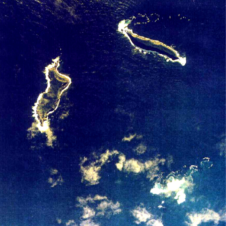 The small islands of Hunga Tonga (upper right) and Hunga Ha'apai (left) are the peaks a large seamount located about 30 km SSE of Falcon Island. The two islands are about 2 km long. They have inward-facing cliffs that represent the W and N remnants of the rim of a largely-submarine caldera lying E and S of the islands. A shoal is visible 3.2 km SE of Hunga Ha'apai and 3 km south of Hunga Tonga and marks the most prominent historically active vent. Aerial photo by Tonga Ministry of Lands, Survey, and Natural Resources, 1991 (published in Taylor and Ewart, 1997).
