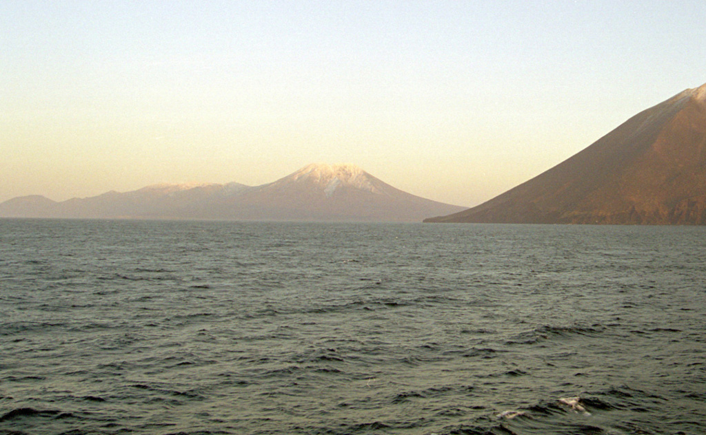 Stokap (center) lies at the SW end of Nishihitokappuyama, an elongated chain of small volcanoes on southern Iturup Island. Nishihitokappuyama consists of a cluster of small NE-SW-trending late-Pleistocene to Holocene cones and craters. Stokap contains 8-10 cones and craters, the largest of which contains a lake. The flank of Etorofu-Atosanupuri is seen in the foreground. Photo by Alexander Rybin, 2001 (Institute of Marine Geology and Geophysics, Yuzhno-Sakhalin).