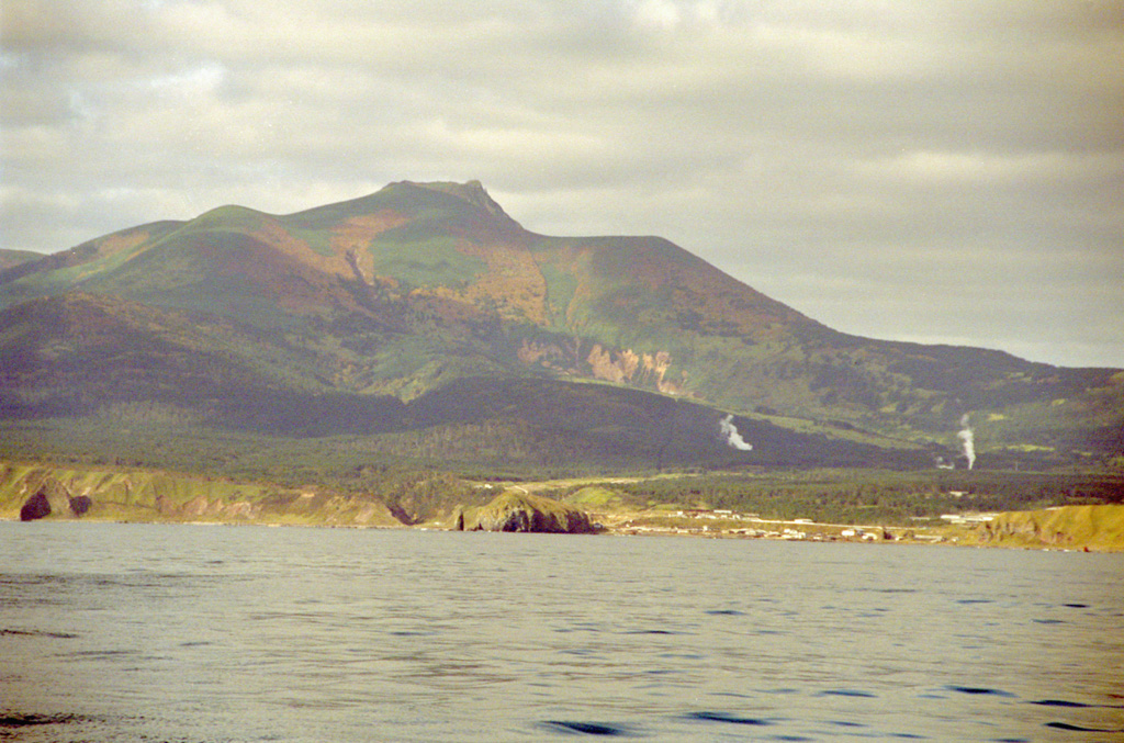 Raususan on the southern part of Kunashir Island towers above the village of Yuzhno-Kurilsk. Steam plumes are visible rising from geothermal wells on the NW flanks, one of several geothermal fields across the volcano. The edifice seen in this view is within a 6-7 km wide caldera.  Photo by Alexander Rybin, 2001 (Institute of Marine Geology and Geophysics, Yuzhno-Sakhalin).