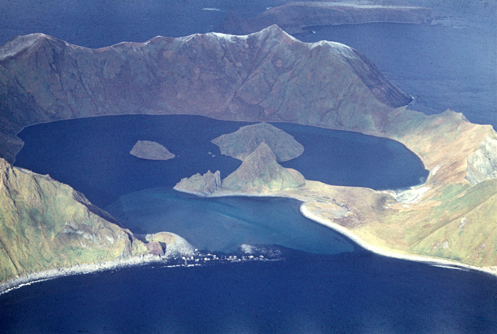The 1.6-km-wide caldera of Ushishur volcano opens towards the south and formed during an eruption about 9,400 years ago. Two post-caldera lava domes that erupted sometime after a 1769 visit of Captain Snow form islands in the caldera bay. Two older domes in front of the islands are joined by a sand bar to the SE caldera wall. A northern island (top) consists of a portion of the flanks. Photo by R. Bulgakov, 1990 (Institute of Marine Geology and Geophysics, Yuzhno-Sakhalin).