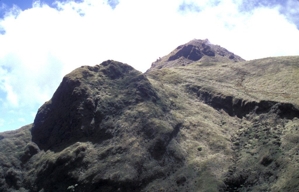 The steep-sided lava dome at the left is Aileron, which was formed about 9700 years ago.  The back side of the dome was cut by the latest of three major edifice-collapse events at Mount Pelée.  The eastern rim of l'Etang Sec, the current summit crater, cuts horizontally across the photo at the upper right in front of the 1929 dome on the right horizon. Photo by Lee Siebert, 2002 (Smithsonian Institution).