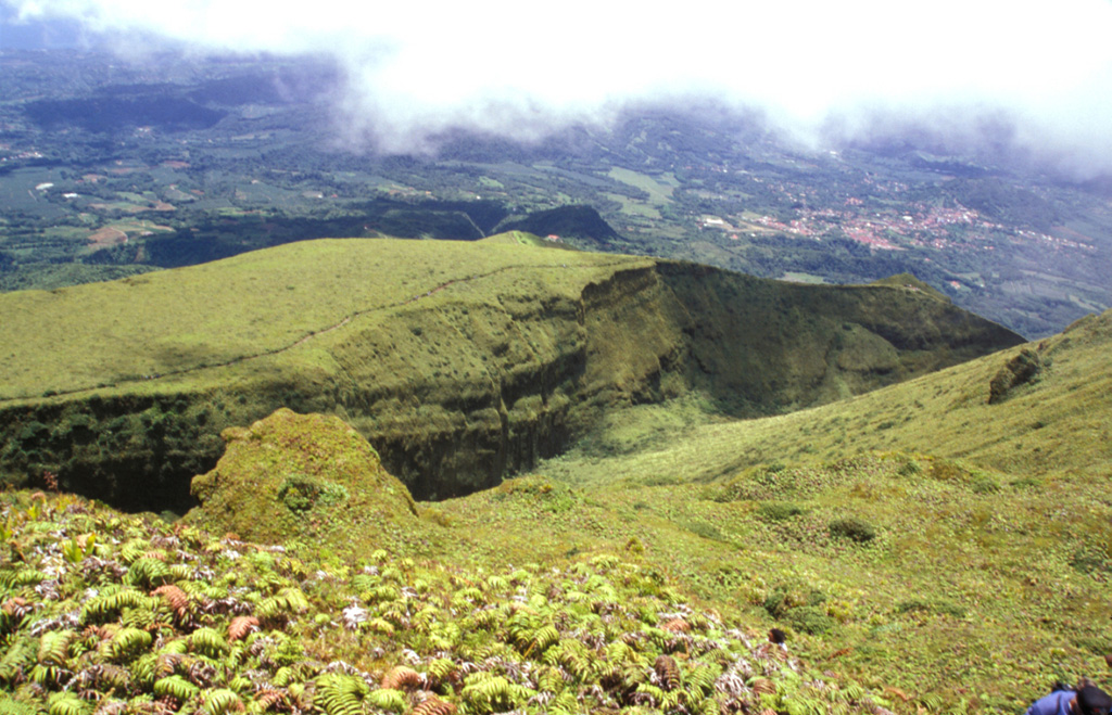 This view from the summit of Mount Pelée shows the eastern rim of l'Etang Sec, the current summit crater of Mount Pelée.  The 1902 and 1920 lava domes fill much of this crater.  The town with reddish roofs at the far right is Morne Rouge, affected by pyroclastic flows from the 1902 eruption. Photo by Paul Kimberly, 2002 (Smithsonian Institution).