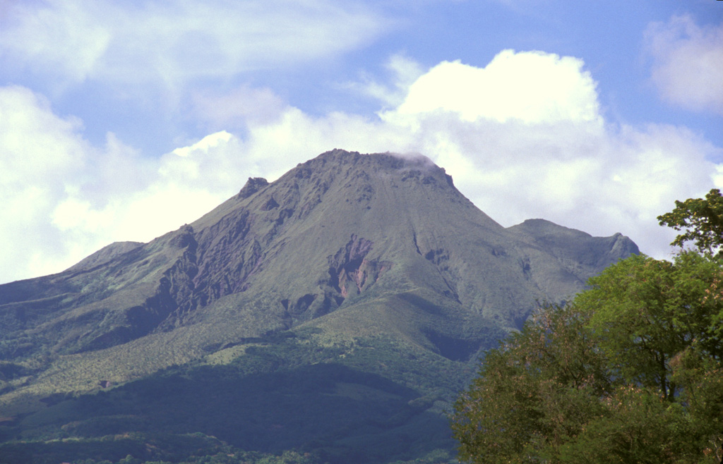 The 1929 lava dome forms the summit of Mount Pelée in this telephoto view from St. Pierre.  The modern volcano was constructed within a scarp produced by collapse of the volcano about 9000 years ago.  The irregularity on the right-hand flank is part of the eastern summit crater rim and the Aileron lava dome, which erupted about 9700 years ago.  Photo by Paul Kimberly, 2002 (Smithsonian Institution).