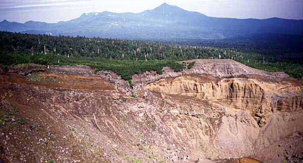 Ruruidake is composed of the cone on the horizon and the gently sloping Smirnov to the left. It is located at the NW tip of Kunashir Island. Smirnov has been extensively eroded by glaciers and contains young pyroclastic flow deposits and lava domes. The late-Pleistocene volcano has an active fumarole field on its western flank. The crater in the foreground is the northern crater of the 1973 eruption of Chachadake volcano to the SE.  Copyrighted photo by Yoshihiro Ishizuka, 1999 (Japanese Quaternary Volcanoes database, RIODB, http://riodb02.ibase.aist.go.jp/strata/VOL_JP/EN/index.htm and Geol Surv Japan, AIST, http://www.gsj.jp/).