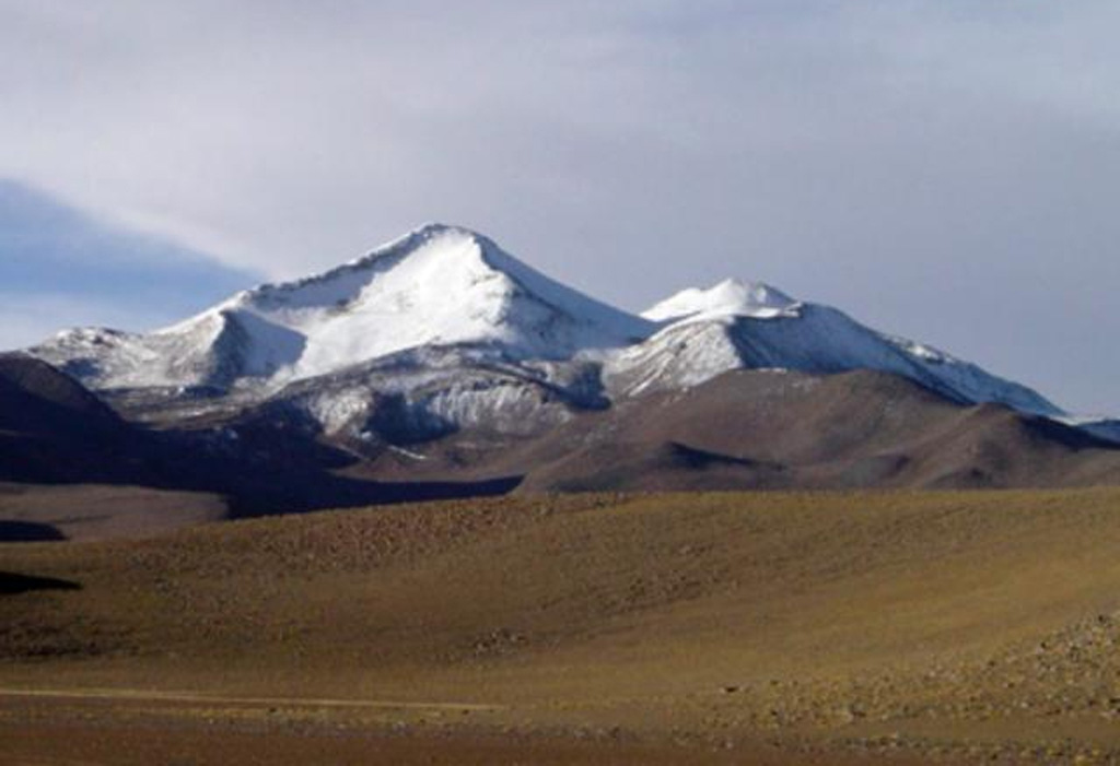 Snow-capped Uturuncu, the highest peak of SW Bolivia, rises to 6008 m.  Andesitic and dacitic lava flows dominate on Uturuncu, seen here from the south.  Although andesitic and dacitic lava flows display well-preserved flow features, youthful-looking summit lava flows show evidence of glaciation.  Two active sulfur-producing fumarole fields are located near the summit. Large-scale ground deformation observed beginning in May 1992, along with recently detected seismicity, indicates that a magmatic system is still present. Photo by Steve Sparks, 2003 (University of Bristol).