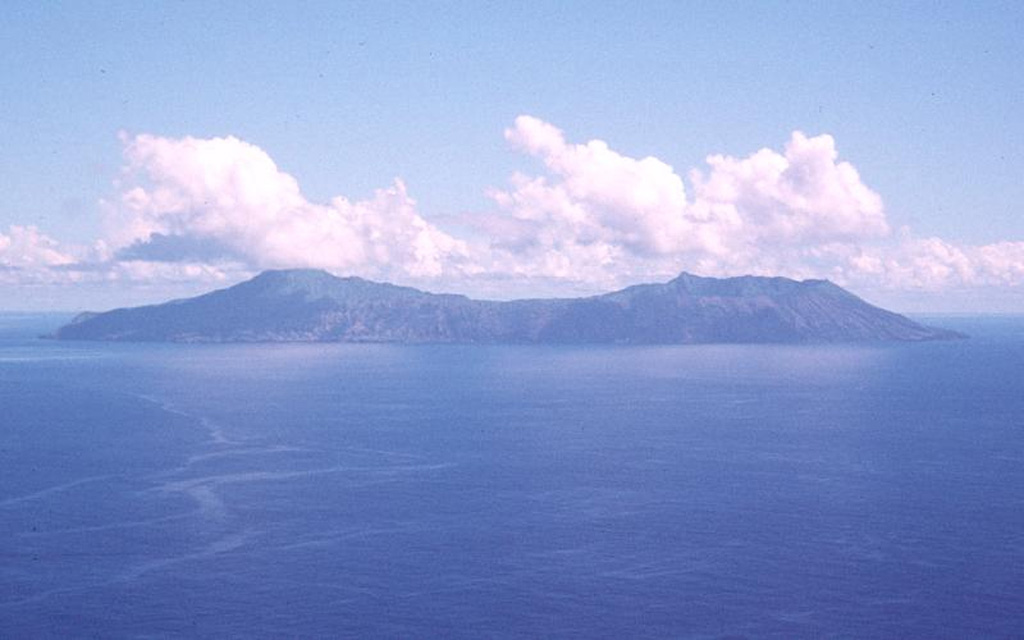 The two coalescing volcanoes forming the elongate 9-km-long island of Anatahan in the central Mariana Islands are seen here from the S. The low point in the center of the island results in part from overlapping 2.3 x 5 km calderas, the largest in the Mariana Islands. The larger western caldera is 2.3 x 3 km and extends eastward from the summit of the western volcano (left). The volcano's first historical eruption in 2003 took place from a small crater within the 2-km-wide eastern caldera. Photo courtesy of U.S. Geological Survey, 1994.