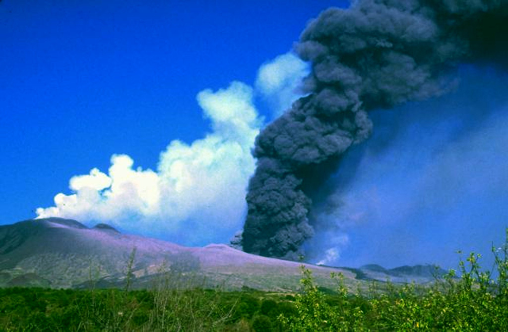 The southern vents of Etna viewed from the SW in the early afternoon of 28 October 2002. From left to right the image shows the summit craters emitting white gas plumes, the cone of Mt. Frumento Supino, vents giving off a dark ash plume, the lower lava vent emitting a faint white plume, new lava flows (dark narrow band), the 2001 cone, and Montagnola cone. Explosive activity began on 26 October and lasted until 28 January 2003. Lava flows cut across roads on the volcano's flanks, causing substantial damage. Photo by Jean-Claude Tanguy, 2002 (University of Paris).