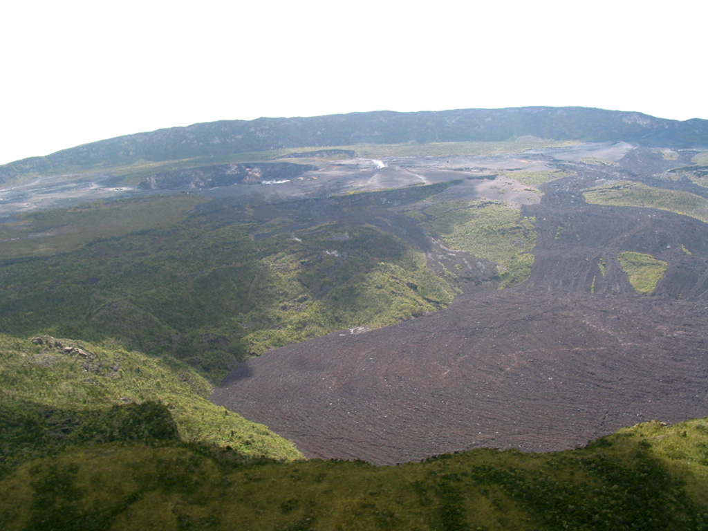 The summit of Nyamuragira volcano is truncated by 2 x 2.3 km wide caldera whose floor is partially covered by unvegetated historical lava flows. This view from above the SW caldera rim shows a crater on the far side of the caldera (upper left) that was the site of a lava lake, active since at least 1921, which drained in 1938 at the time of a major flank eruption.  Photo by Simon Carn, 2004 (TOMS Volcanic Emissions Group, University of Maryland, Baltimore County).