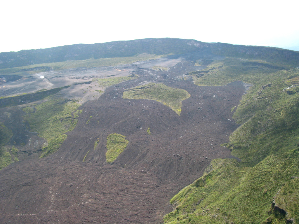 Recent lava flows surround vegetated kipukas on the caldera floor of Nyamuragira volcano in this view from the SW caldera rim. The 2 x 2.3 km wide caldera has walls about 100 m high. A prominent scarp in the middle of the caldera floor at the far left is the rim of a partially buried crater. Historical eruptions have frequently modified the morphology of the caldera floor. Photo by Simon Carn, 2004 (TOMS Volcanic Emissions Group, University of Maryland, Baltimore County).