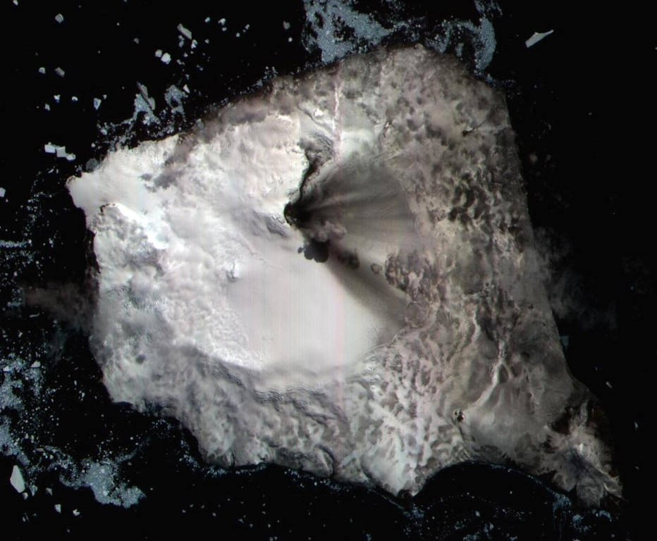 This 7 December 2003 ASTER satellite image shows Montagu island with recent volcanic deposits visible across the icy surface of the island from Mount Belinda. The smooth ice and snow south of Belinda reflects 6 km wide caldera. A dark lava flow can be seen extending NE from the summit vent (towards the top). The dark feature extending south from the summit (towards the bottom right) is the shadow of a small ash plume rising to the southeast. Ash deposits are visible in a fan right of the central vent (E). ASTER satellite image, 2003 (National Aeronautical and Space Administration, courtesy of ASTER science team).