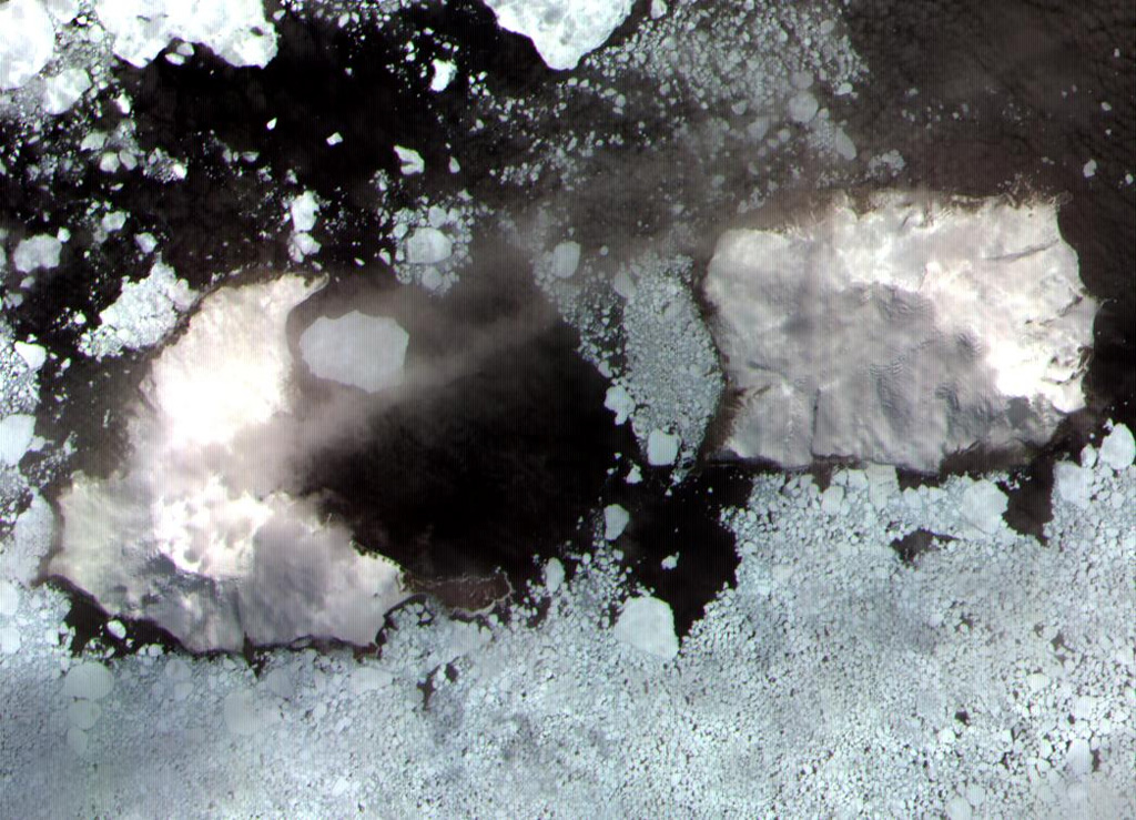 Thule (left) and Cook (right) islands are seen surrounded by ice floes in this ASTER satellite image.  Douglas Strait, the ice-free area in the center of the image, is underlain by a 4.3 x 4.8 km wide caldera between the two volcanic islands.  A third stratovolcano forms Bellingshausen Island, just out of view to the right.  The Thule Islands lie at the southern end of the South Sandwich island arc bordering the Scotia Sea and consist of three stratovolcanoes constructed along an E-W-trending line.   ASTER satellite image, 2003 (National Aeronautical and Space Administration, courtesy of ASTER science team).