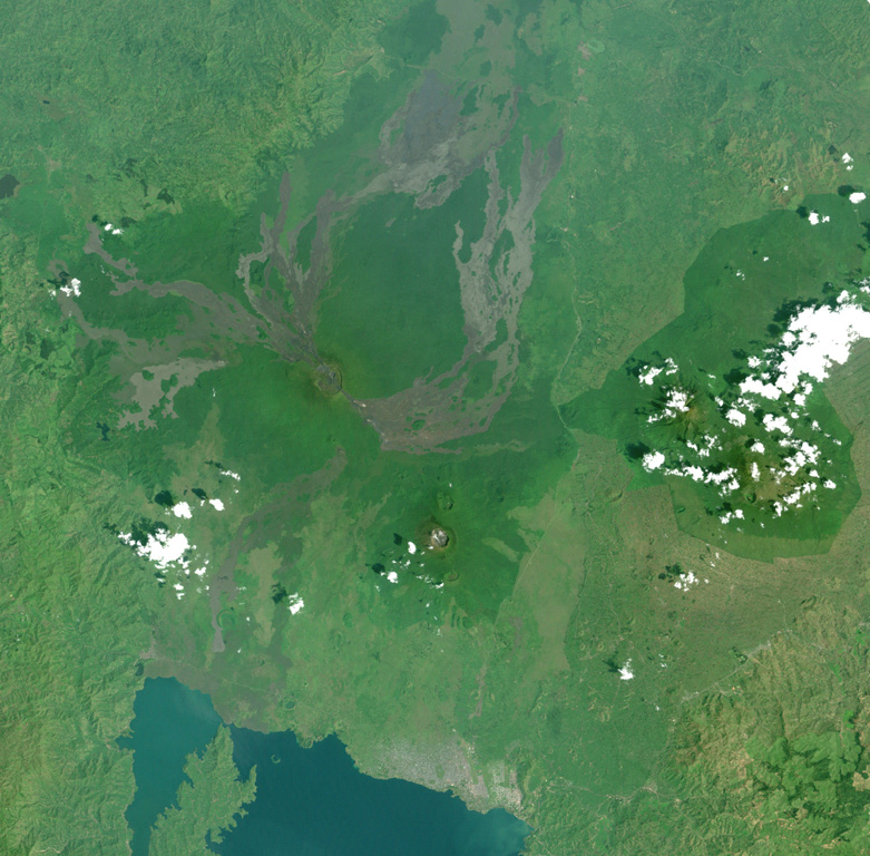This Landsat image shows a portion of the East African Rift north of Lake Kivu (bottom), with N to the upper left. Unvegetated lava flows descend from vents on the summit and flanks, some reaching the shores of Lake Kivu. The forested volcano below and to the right is Nyiragongo, a volcano that frequently contains an active lava lake. Lava flows from flank fissures in 2002 cut across the city of Goma (the light-colored area at the right-hand side of the lake). NASA Landsat image, 2001 (courtesy of Simon Carn, TOMS Volcanic Emissions Group, Univ. Maryland, Baltimore County).