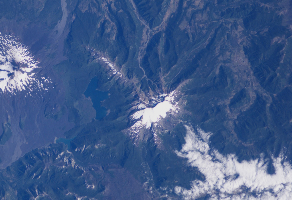 The glaciated Sierra Nevada volcano (center) is an andesitic to basaltic stratovolcano that lies about 15 km NE of Llaima volcano (far left).  A snow-capped 7-km-long, E-W zone of fissure vents is visible above and to the left of Sierra Nevada near Laguna Conquillio, whose shores are partially constrained by lava flows from the two volcanoes.  The age of Sierra Nevada has been considered to be late-Pleistocene or late-Pleistocene to Holocene.  NASA International Space Station image ISS006-E-40420, 2003 (http://eol.jsc.nasa.gov/).
