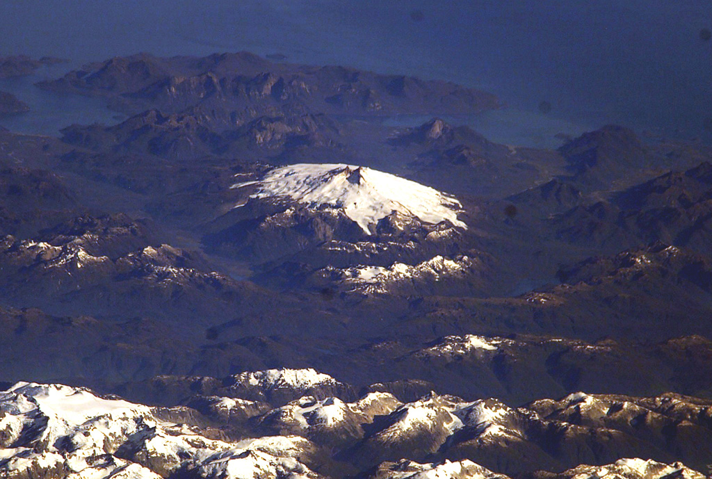 Glacier-clad Melimoyu is the prominent stratovolcano in this oblique NASA International Space Station image looking west toward the Corcovado Gulf.  The volcano has an ice-filled 8-km-wide caldera that is drained by a glacier through a notch in the NE rim.  The basaltic-andesite volcano is Pleistocene-Holocene in age. NASA International Space Station image ISS006-E-42370, 2003 (http://eol.jsc.nasa.gov/).