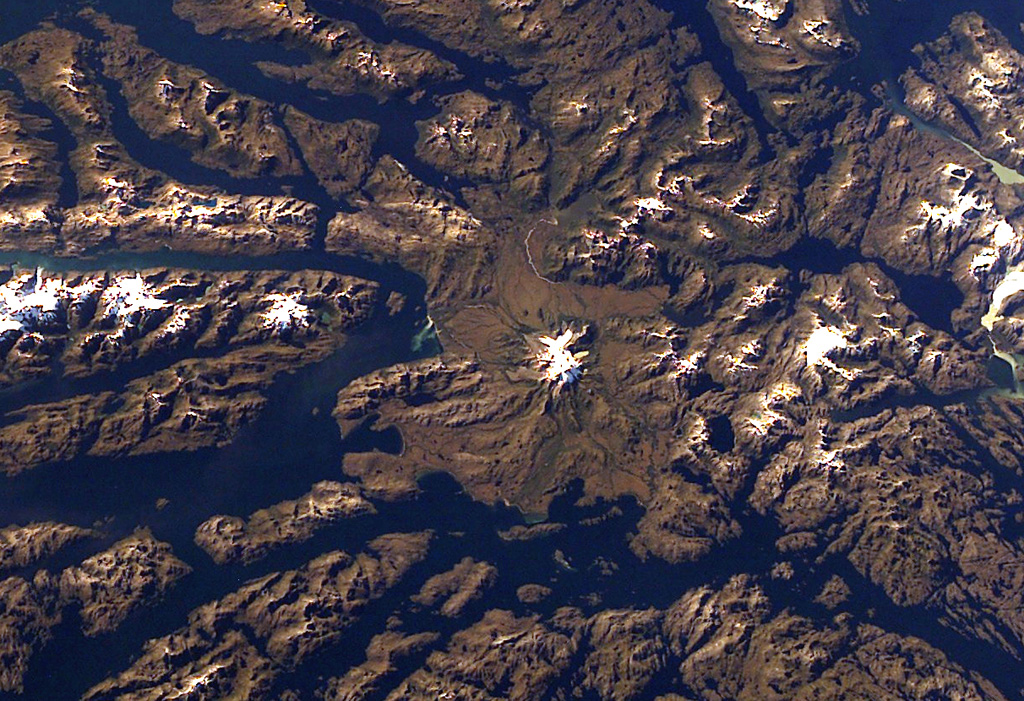 Ice-covered Mount Burney occupies the NW part of the Muñoz Gomera Peninsula in the spectacular glaciated Patagonian fjord region of southern Chile.  The volcano lies near the center of this NASA International Space Station image (with north to the left).  The rugged extensively glaciated topography surrounding the 1758-m-high Monte Burney is smoothed by volcaniclastic deposits from the volcano. NASA International Space Station image ISS006-E-41451, 2003 (http://eol.jsc.nasa.gov/).