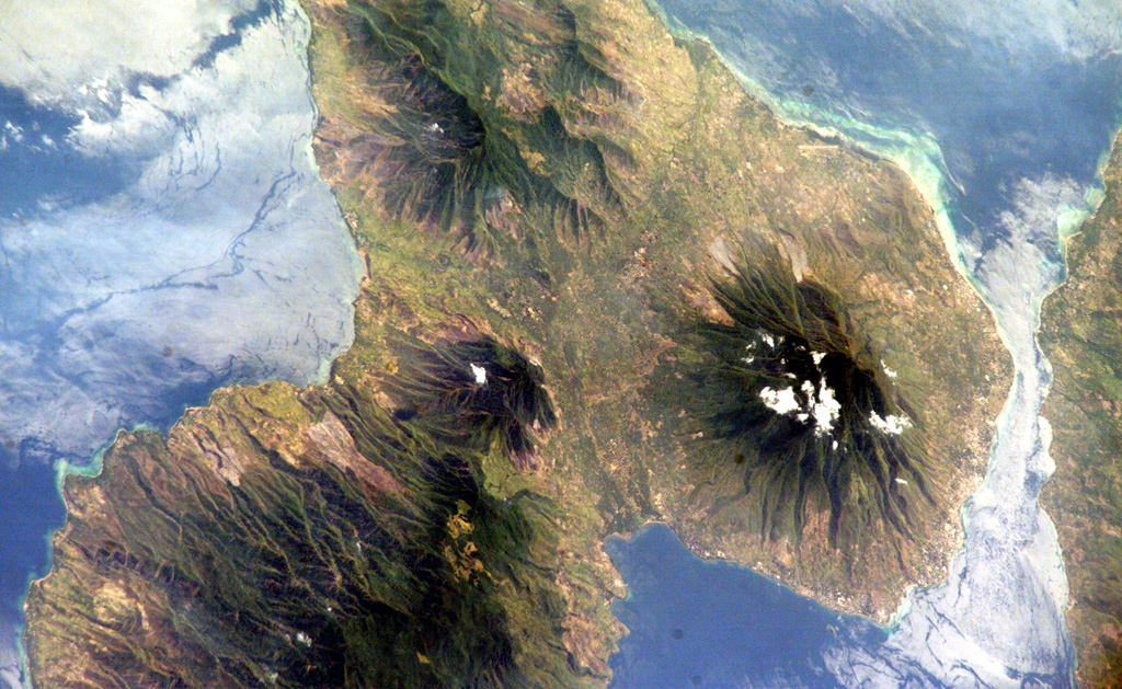 A lone cloud rises above Ilikedeka volcano near the center of this NASA International Space Station image of the NE end of Flores island.  The Riang Kotang fumarole field consists of two fumarolic areas located at the northern foot of Quaternary Ilikedeka volcano, along the saddle between it and the volcanic massif at the top of the image.  Hot springs are located along the SW side of Oka Bay (bottom) and Hadang Bay on the NW coast. NASA International Space Station image ISS005-E-17557, 2002 (http://eol.jsc.nasa.gov/).