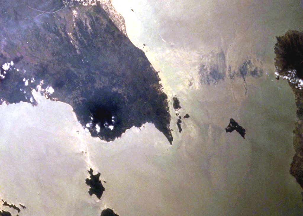 The dark-colored forested area with scattered clouds on the rounded peninsula left of the sharp-tipped Tua Peninsula forming the SE tip of Sumatra is Rajabasa volcano. The NW tip of Java (right) lies across the Sunda Strait in this NASA Space Shuttle image with north to the upper left. The low, conical volcano has a well-preserved 500 x 700 m summit crater with a swampy floor. The age of its most recent eruptions is not known, although fumarolic activity occurs on the foot and flanks of the volcano. NASA Space Shuttle image STS106-705-29, 2000 (http://eol.jsc.nasa.gov/).