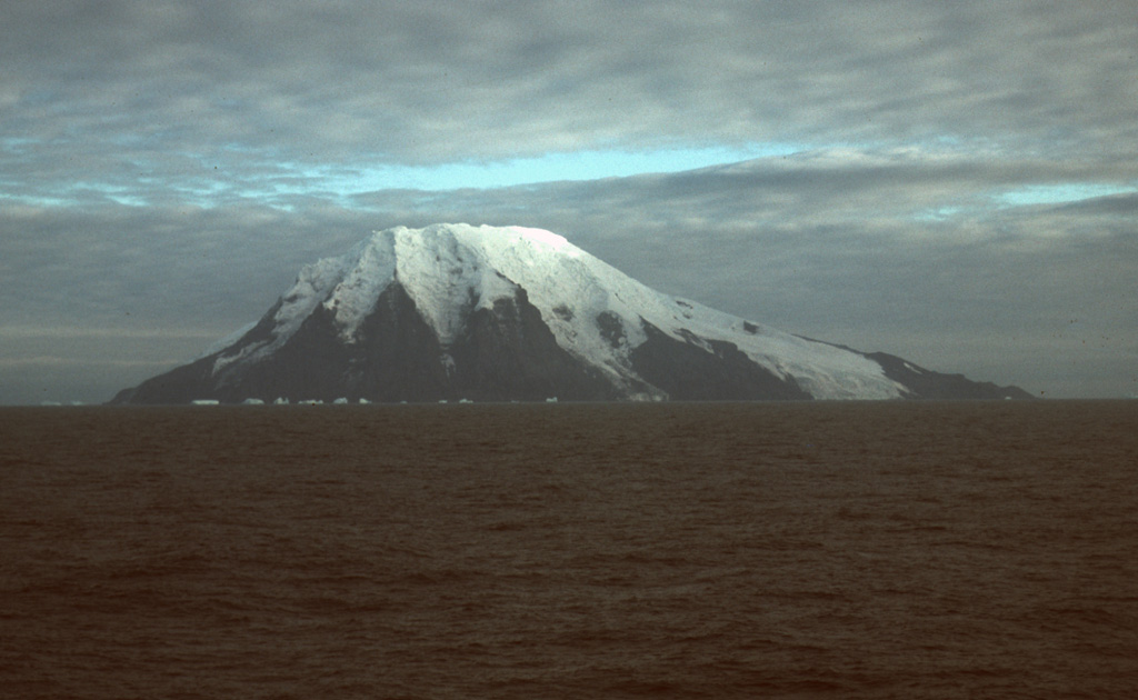 Glaciers descend the steep southern face of Visokoi Island from the flat-topped summit of Mount Hodson. Wordie Point (left) and Irving Point (right) lie respectively at the west and east sides of the 5.5 x 7 km wide island. The sea cliffs comprise interbedded lavas and pyroclastics. The cliffs at Wordie Point are formed by thick columnar-jointed lavas. Numerous basaltic scoria cones were constructed on the lower flanks of the island, including at Irving Point, and are thought to represent the most recent activity. Photo by John Smellie (British Antarctic Survey).