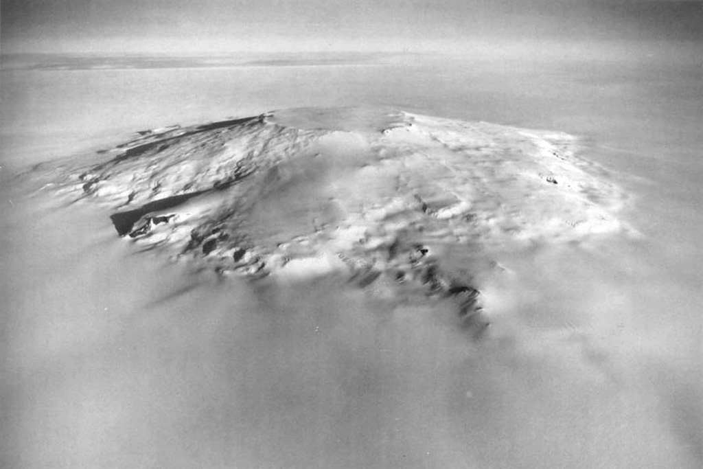 This aerial view looks northeast across the trachytic shield volcano Mount Takahe, with an ice-filled 8-km-diameter caldera at the summit. The approximately 30-km-wide edifice rises about 2,000 m above the surrounding ice sheet. Eruption deposits indicate both subaqueous and subaerial eruptions, and include lavas and tephra. Möll Spur (right of center) is a prominent steep ridge of lava produced in two sequences at about 34 and 17 ka. The most recent eruption occurred around 5.6 ± 0.8 ka, producing widespread tephra distribution across West Antarctica. U. S. Navy photo TMA 1718 F33 022.