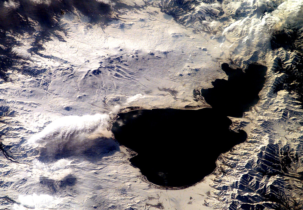 Small cones and lava domes dot the surface of snow-covered Ghegam Ridge (upper left), located west of Lake Sevan (right) in west-central Armenia. North lies to the upper right in this NASA International Space Station image. The volcanoes and associated lava flows cover a 65-km-long, 35-km-wide area west of Lake Sevan and are concentrated along three NNW-SSE-trending alignments. Lava flows from the central and eastern clusters flowed into Lake Sevan at the upper left-hand side of the lake. NASA International Space Station image ISS006-E-42481, 2003 (http://eol.jsc.nasa.gov/).