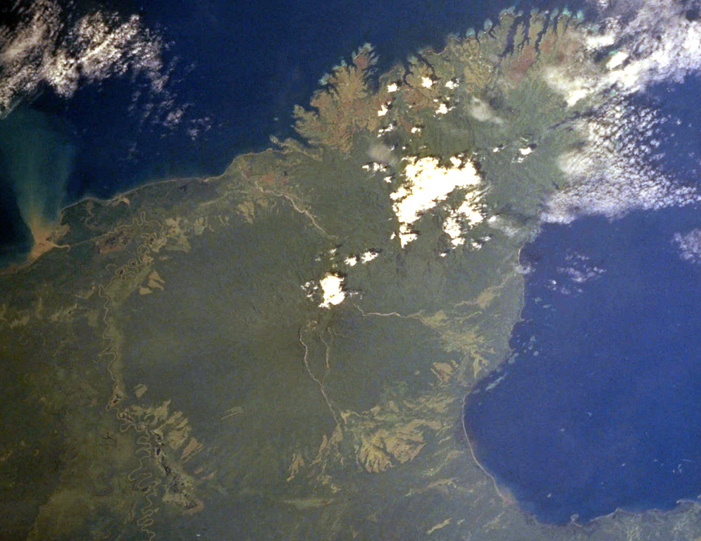 The forested volcanic massif at the center of the image is Mount Victory, which occupies the lower part of a peninsula SW of Cape Nelson (upper right). To the NE it abuts the deeply dissected Pleistocene Mount Trafalgar volcano, its summit draped by the larger cloud banks. The summit crater of Mount Victory contains a breached crater and several lava domes. The only confirmed historical activity of Mount Victory was a long-term late-19th to early 20th-century eruption that produced pyroclastic flows that reached the coast. NASA Space Shuttle image STS093-710-19, 1999 (http://eol.jsc.nasa.gov/).
