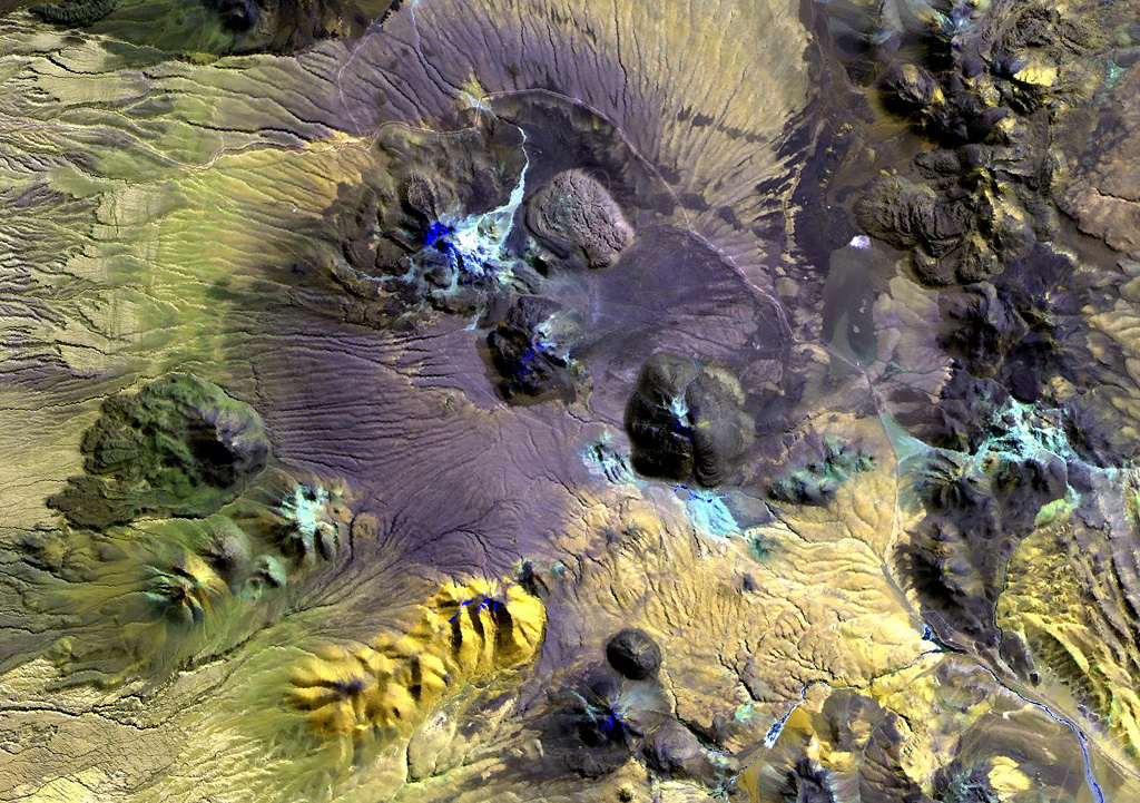 Erosional furrows cut outflow sheets of Pleistocene ignimbrites of the Purico Complex that were erupted from a postulated 10 x 20 km ring fracture.  The light-colored dome at the top center is Pleistocene in age, but the youngest lava domes, Cerro Chascón de Purico (center) and Cerro Aspero (the small dome at the bottom center) are of Pleistocene-Holocene age.  The dacitic-to-andesitic Macon stratovolcano of Holocene age lies at the SW end of the complex (far left-center).  The Guayaques volcanic chain lies at the upper right. NASA Landsat image, 1999 (courtesy of Hawaii Synergy Project, Univ. of Hawaii Institute of Geophysics & Planetology).