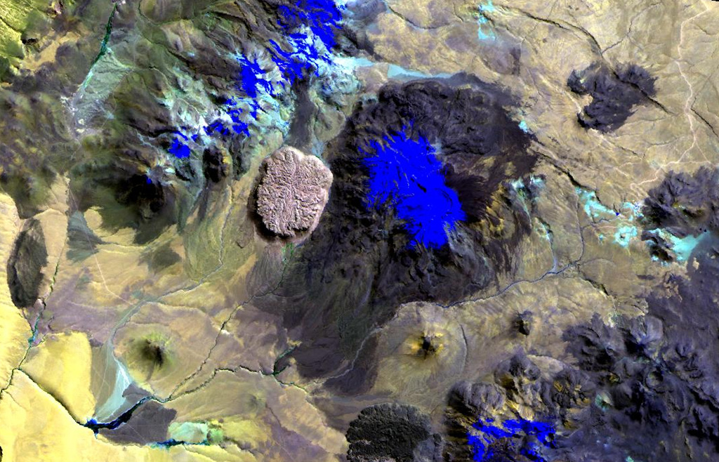 The youthful-looking rhyolitic lava dome, Cerro la Torta (left of center), lies at its western foot of Cerros de Tocorpuri (or Volcán Tocorpuri), a stratovolcano complex on the Chile-Bolivia border.  The circular, roughly 5 cu km Cerro la Torta has a flat-topped surface with wrinkled flow ridges and terminates in steep, talus-covered margins about 150 m high.  The dome has a youthful appearance, but its age is not precisely known.  Snow cover in this Landsat view is deep blue.   NASA Landsat image, 1999 (courtesy of Hawaii Synergy Project, Univ. of Hawaii Institute of Geophysics & Planetology).