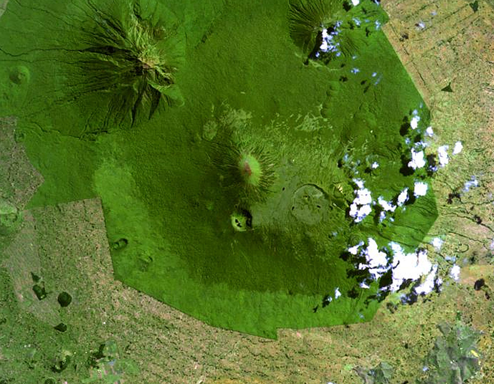 The Karisimbi volcanic complex (center) includes a symmetrical, peaked summit flanked to the SE by the 2-km-wide Branca caldera, which is filled by viscous lava flows and two craters. The smaller Muntango crater is located S of the summit. A broad lava plain composed of flows erupted within the caldera and along a chain of parasitic cones, extends SW. Eroded Mikeno volcano is at the upper left and Visoke volcano at the upper right of this Landsat image. NASA Landsat image, 1999 (courtesy of Hawaii Synergy Project, Univ. of Hawaii Institute of Geophysics & Planetology).