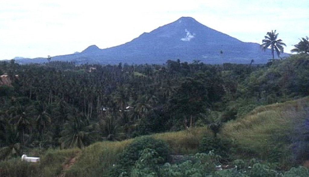 Klabat, seen here from the city of Manado to its west, is an isolated symmetrical stratovolcano that rises to 1995 m near the eastern tip of the northern arm of Sulawesi. It has a shallow lake in its 170 x 250 m summit crater.  No verified historical eruptions have occurred from this volcano, the highest in Sulawesi.   Photo by Thomas Dobat, 1983.