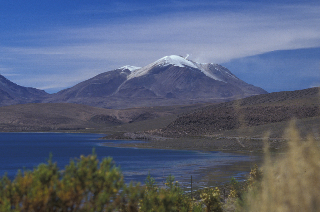 Volcán Guallatiri rises to the SSE beyond Laguna Chungará, and steam rises from a prominent fumarole near its summit.  The symmetrical ice-clad stratovolcano lies at the SW end of the Nevados de Quimsachata volcano group just west of the border with Bolivia and is capped by a central dacitic dome or lava complex. Thick lava flows can be seen on its lower northern and western flanks.  Minor explosive eruptions have been reported from Guallatiri since the beginning of the 19th century, and intense fumarolic activity continues. Photo by Lee Siebert, 2004 (Smithsonian Institution).