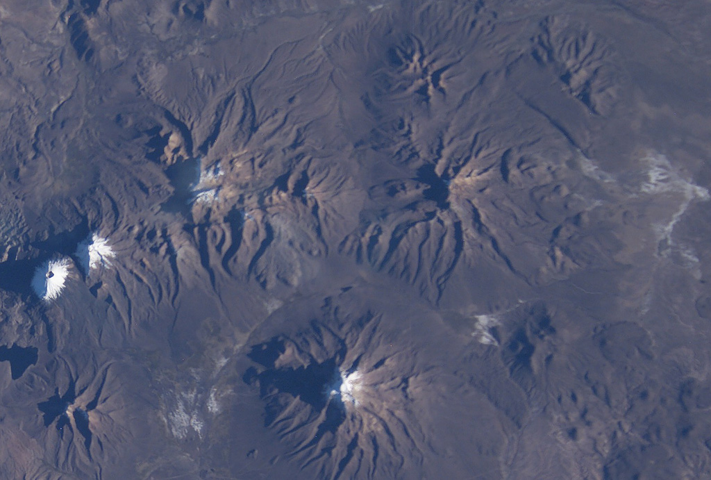 The eroded volcanic massif above and to the right of the center of this NASA International Space Station image (with north to the upper right) is the Nevado Anallajsi volcanic complex.  The basaltic-to-dacitic volcano has been extensively dissected by glaciers.  Younger basaltic lava flows were erupted from a north-flank vent, but the age of this activity is uncertain.  The large volcano at the bottom center is Sajama volcano, also in Bolivia, and the twin snow-capped peaks at the far left-center are Pomerape and Parinacota volcanoes along the Chilean border. NASA International Space Station image ISS009-E-6848, 2004 (http://eol.jsc.nasa.gov/).