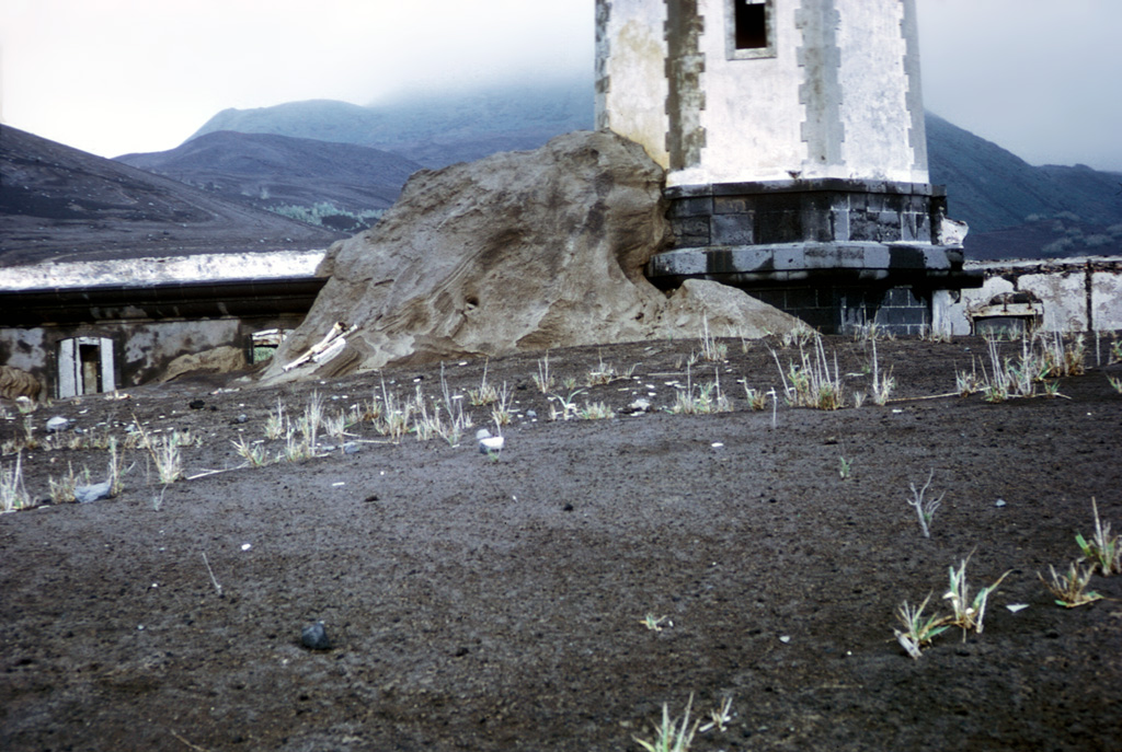 Pyroclastic surge, or base surge deposits from the 1957 phreatomagmatic Capelinhos eruption lap up against a lighthouse near the western coast of Fayal Island in the Azores. Pyroclastic surges produced by magma-water interaction during the Surtseyan eruption nearly buried the lower floor of the lighthouse building. The initially submarine eruption began off the western tip of Fayal, forming a small island that was eventually joined to the main island.  Photo by R.V. Fisher, 1979 (University of California Santa Barbara).