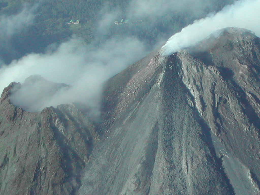 Gas emissions rise from the active Arenal summit crater (Crater C, upper right) in 2003, and a lava flow descends the NE flank to the bottom of the image. Some fumarolic activity is occurring from the pre-1968 crater (Crater D, left). The building at the top left is the Arenal Volcano Observatory. Photo by Eliecer Duarte, 2003 (OVSICORI-UNA).