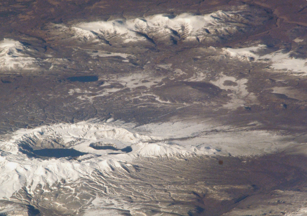 The small, low-angle, snow-free volcano near the center of this NASA International Space Station image (with N to the right) is Ozernoy volcano. This early Holocene cone is dwarfed by the Ksudach caldera to the SE (lower left). NASA International Space Station image ISS005-E-19216, 2002 (http://eol.jsc.nasa.gov/).