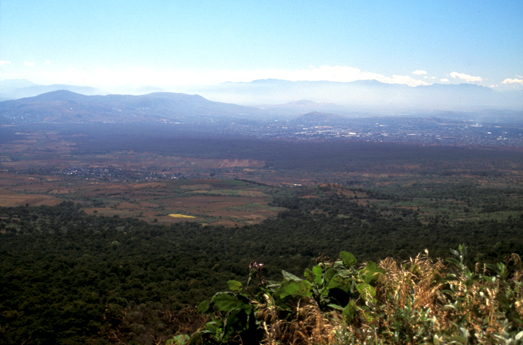 The darker forested area in the center of this photo, extending from the middle right almost across the broad valley floor, is the Texcal lava flow. This lava flow traveled 24 km S onto the Cuernavaca plain after being erupted about 4,200 years ago from the Guespalapa scoria cone. Unlike the Pelado or Chichinautzin eruptions, the Guespalapa eruption did not produce a small shield, but rather one of the longest lava flows of the Sierra Chichinautzin. Photo by Lee Siebert, 2004 (Smithsonian Institution).