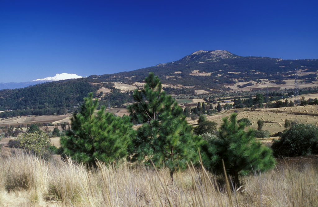 The Cuautzin lava dome (right horizon) north of the crest of the Sierra Chichinautzin, with cnow-capped Iztaccihuatl volcano on the left horizon. It formed between about 7,360 and 8,225 radiocarbon years ago, producing lava flows and block-and-ash flow deposits around the dome. Cuautzin means "Seat of the Eagle" in the Nahuatl language.  Photo by Lee Siebert, 2004 (Smithsonian Institution).