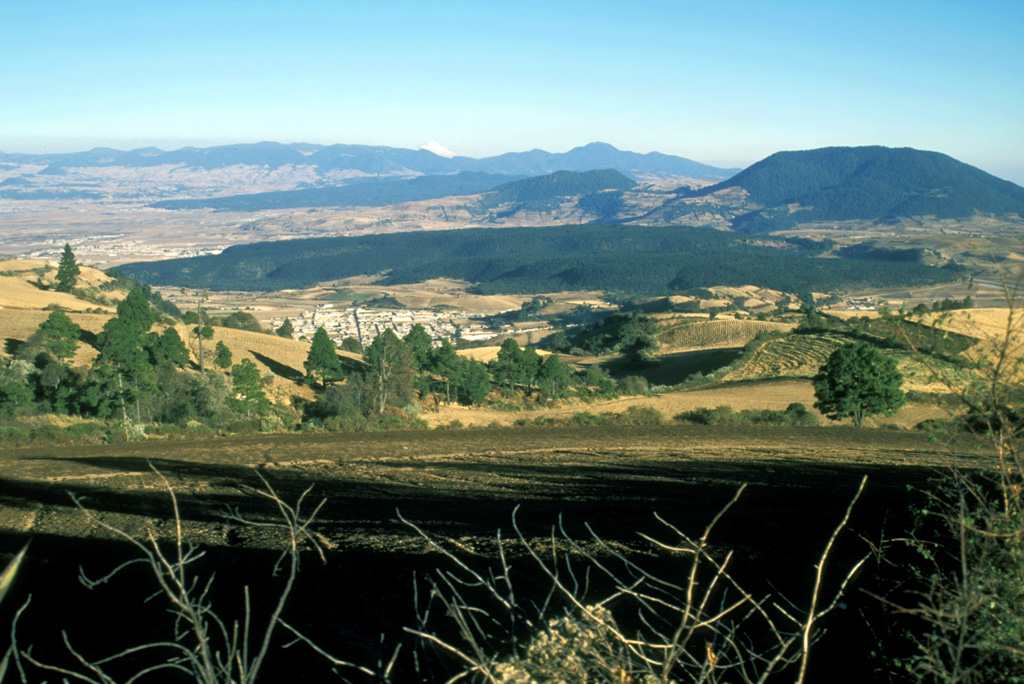 The broad forested ridge in the center of this photo is the Tenango lava flow, which was erupted about 8,500 radiocarbon years ago from an E-W-trending fissure at the western margin of the Chichinautzin volcanic field. It forms a prominent isolated mesa on which the fortified city of Teotenango with its many pyramids and courts was built by the Matlatzinca people about 1000 BCE. Photo by Lee Siebert, 2004 (Smithsonian Institution).