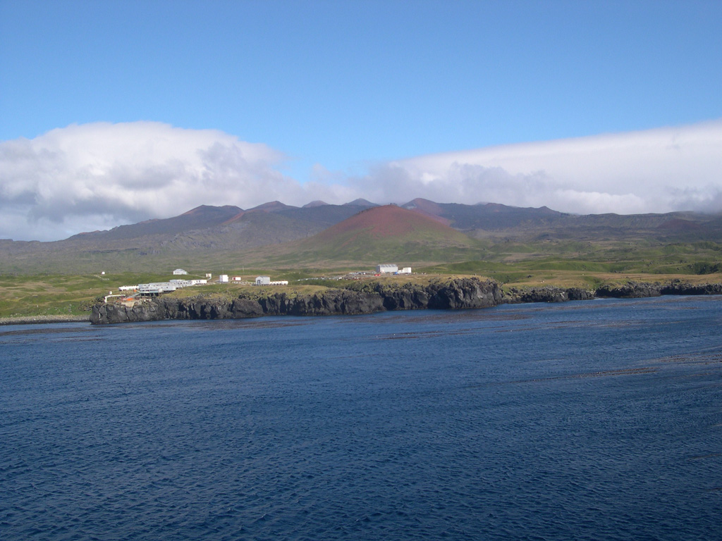 Marion Island, South Africa's only historically active volcano, is seen from the NE with the meteorological station in the foreground. The red scoria cone is the lowest of a NE-trending chain of cones extending from the near the summit of the shield volcano. The meteorological station sits on Pleistocene lava flows. The island includes about 150 scoria cones and coastal tuff cones, most of which formed during the Holocene. The first historical eruption took place in 1980. Photo by Ian Meiklejohn (University of Pretoria).