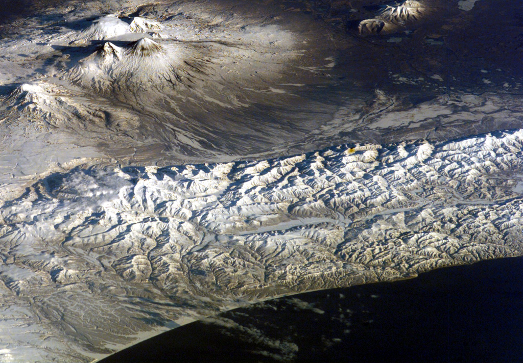 A group of isolated cinder cones lies near the Pacific Coast of Kamchatka at the lower right portion of this NASA International Space Station image (with north to the upper right).  The age of the cones ranges from mid-Pleistocene to perhaps early Holocene.  Large stratovolcanoes of the Kliuchevskoi group are visible at the upper left and include Zimina (far left), the twin sharp-topped peaks of Kamen and Kliuchevskoi, and above them the Ushkovsky massif.  The two volcanoes at the upper right are Zarechny and Kharchinsky, of Pleistocene age. NASA International Space Station image ISS004-E-13794, 2002 (http://eol.jsc.nasa.gov/).