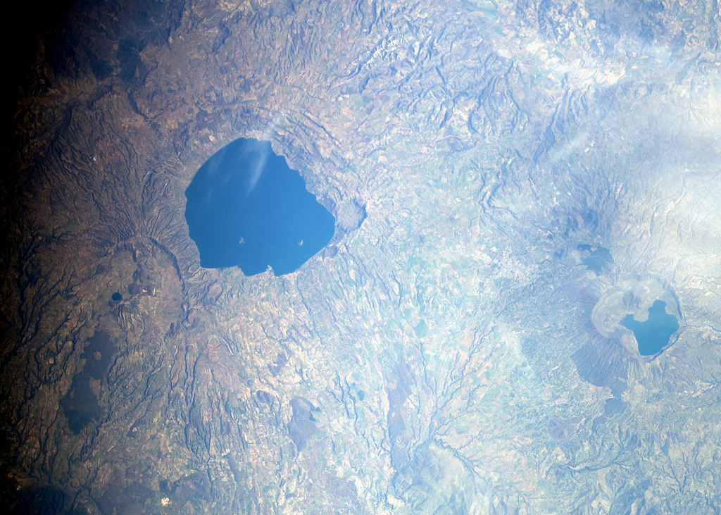 Three large calderas are seen in this NASA International Space Station image (with north to the upper left) of the Vulsini volcanic complex in central Italy. The 16-km-wide Lake Bolsena (left-center) was formed during major Pleistocene explosive eruptions at about 300,000 years ago and the 8 x 11 km wide Latera caldera (below and to the left of Bolsena) about 160,000 years ago. Post-caldera volcanism produced scoria cones and lava flows (lower left) until recent times. Pleistocene Lake Vico in the Cimini Mountains lies at the right-center. NASA International Space Station image ISS006-E-36701, 2003 (http://eol.jsc.nasa.gov/).