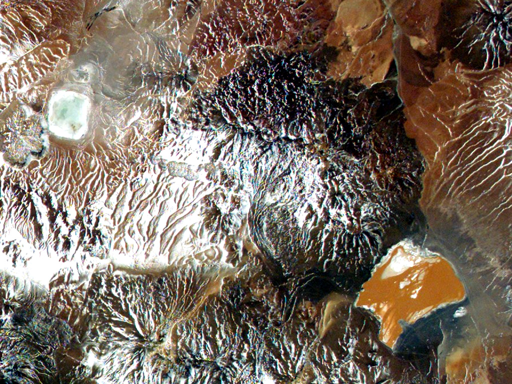 The large dark-colored area above orange-colored Laguna Colorada in this NASA International Space Station image (with north to the upper left) is Volcán de Jorcada.  This elongated fissure-controlled volcanic massif contains more than 50 craters, small stratovolcanoes, and lava domes erupted along four fissures covering an area of 230 km2.  Activity has migrated to the north, and the youngest fissure, on the NW side of the complex, produced a number of snow-dusted cones visible left of the center of this image. NASA International Space Station image ISS005-E-8788, 2002 (http://eol.jsc.nasa.gov/).