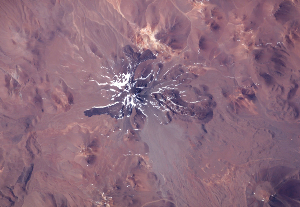 The world's highest historically active volcano, Llullaillaco, sits astride the Chile-Argentina border in this NASA International Space Station image (with north to the upper right). A well-preserved summit cone was the source of prominent lava flows that are older than they appear in this image. The hilly terrain at the lower right was produced by a major debris avalanche about 150,000 years ago that swept eastward into Argentina and diverges around the north and south sides of the older Cerro Rosado stratovolcano (extreme lower right). NASA International Space Station image ISS006-E-13814, 2003 (http://eol.jsc.nasa.gov/).