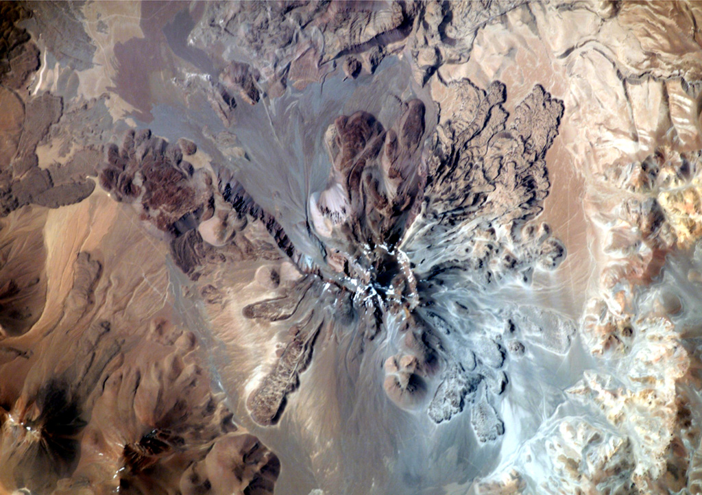 This dramatic NASA International Space Station image (with north to the upper right) is of Socompa volcano. A large horseshoe-shaped caldera breached to the NW was the source of a major debris avalanche about 7,000 years ago that extended beyond the upper left margin of the image. Young dacitic lava domes and flows partially fill the collapse amphitheater, and prominent lava flows with flow levees are visible on the outer flanks. NASA International Space Station image ISS003-E-5375, 2001 (http://eol.jsc.nasa.gov/).